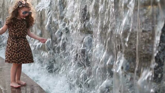 barefoot girl in sunglasses and dress touches water of waterfall
