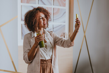 Woman using smartphone drinking green smoothie with bamboo straw in the office