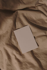 Blank paper sheet card with mockup copy space on crumpled beige bed blanket with soft warm sunlight...