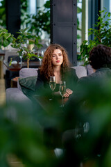 Fototapeta premium portrait of young upset curly woman quarreling on business meeting with colleague or on date with man with glasses of champagne