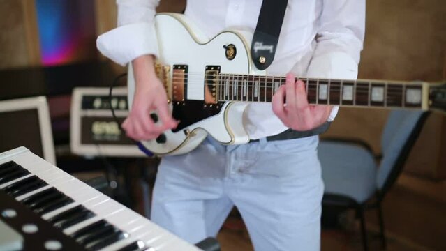 Hands of guitarist playing guitar next to keyboards in studio