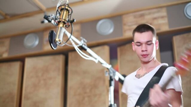 Glamorous boy plays guitar next to speaker in recording studio