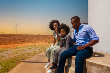 Three black African American parents and daughters, family sitting at a wind turbine station in a...