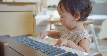 cute little Asian toddler girl kid try playing piano at home, child having fun with learning to play music instrument. Education, skills concept