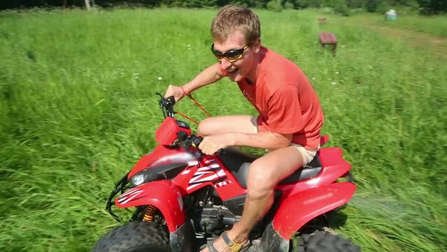 Happy young man rides around circle on red quad bike