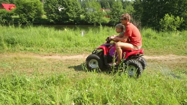 Happy young man with daughter rides around circle on quad bike