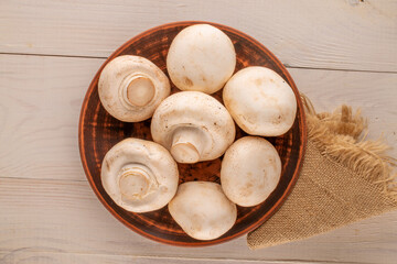 Several fresh mushrooms in a clay plate on a wooden table, macro, top view.
