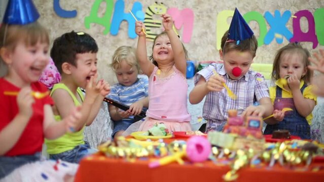 kids sit at red table with cake and throw confetti