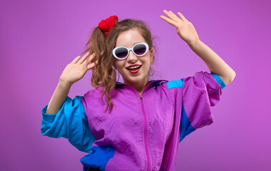 Cool teenager. Fashionable DJ girl in colorful trendy jacket and vintage retro sunglasses enjoys style of 80s-90s vibes. Teenager at disco party. Young fashion model on pink background.