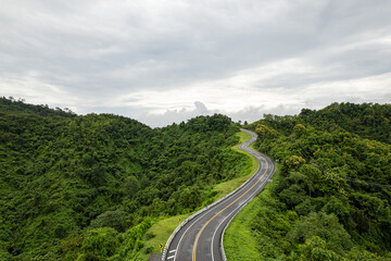 Aerial view of countryside road passing through the green forest and mountain in Thailand.