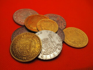 Spanish gold and silver coins, Shields and Reales, on a red background