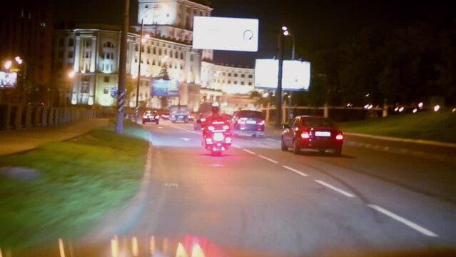 Cars and motorcycle ride under bridge on night street