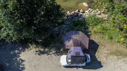 Car with a roof tent and a large awning by a river
