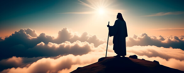Silhouette of Jesus Christ on top of a hill looking at the sunset. Banner format.