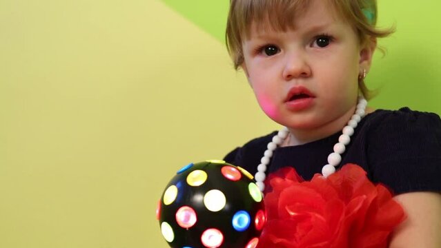 Little girl in blue dress and white beads holds ball with lights