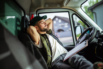 A tired truck driver takes a break from driving and rests in his truck