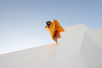 Fototapeta premium Girl in orange dress on white background with blue sky