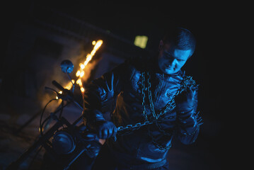 Motorbiker in the black leather jacket with the spikes in the blue light on the burning fire...