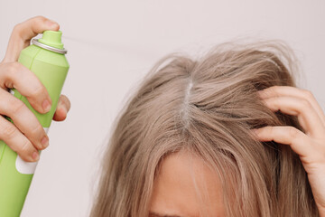 Cropped shot of a young woman with dirty greasy hair spraying dry shampoo on the roots of her hair...