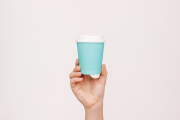 Woman's hand holding blue eco paper cup with white lid with tea or coffee isolated on light...