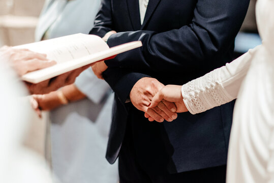 Detalle de una pareja de novios agarr&aacute;ndose de las manos en el altar durante la ceremonia de casamiento frente al sacerdote. Concepto del sacramento del matrimonio en la iglesia Cat&oacute;lica