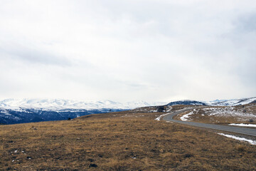 Empty asphalt road winding among the mountains, leading to the snowy mountains