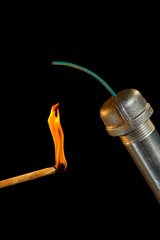 A metal pipe bomb with lit match against a black background
