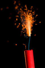 A closeup of sparks flying from lit fuse on a red stick of dynamite again black background