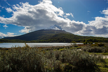Cloudy landscape of a snow-capped mountain with pine forest and a lake at its base. Cerro Condor, Tierra del Fuego National Park.