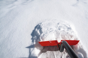A red snow shovel pushing snow with motion blur