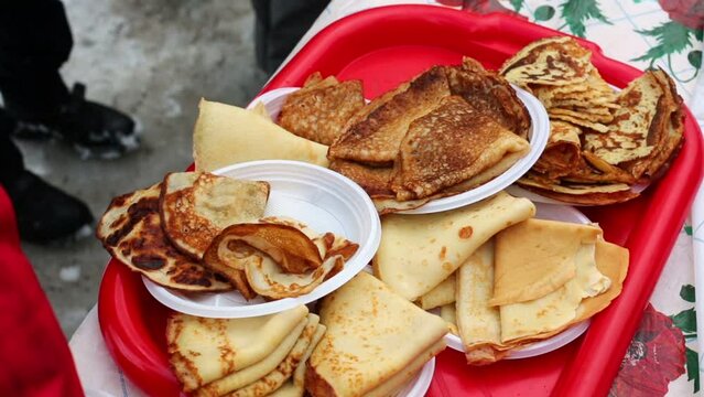 People eat pancakes from red tray standing on the table outdoor