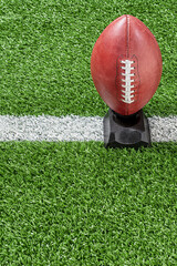 An American football on kicking tee with yard line