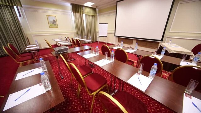 White screen for projector, tables and chairs in meeting hall