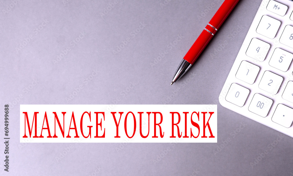 Poster manage your risk text written on a gray background with pen and calculator