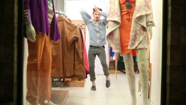 Young handsome man dances in showcase of small clothing store