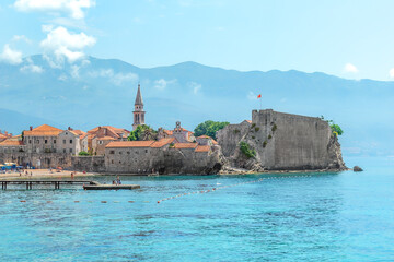 Seascape with the fortress of the Old Town of Budva and the spire of the chapel of The Church of Sveti Ivan, Montenegro. Plaza Ricardova Glava beach and Adriatic Sea coastline in a tourist city