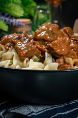Pasta with beef stew in black bowl.