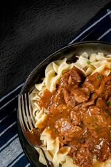 Pasta with beef stew in black bowl.