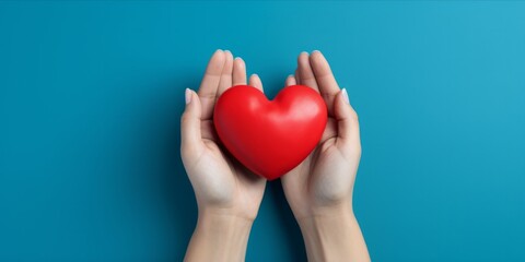 Hands holding a red heart against a blue background.
