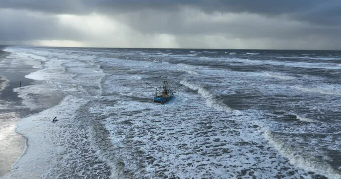 Aerial drone view of a stranded small shrimp trawler fishing boat at a beach.