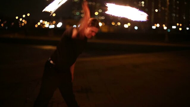 Young man juggles with burning mace during fire show.