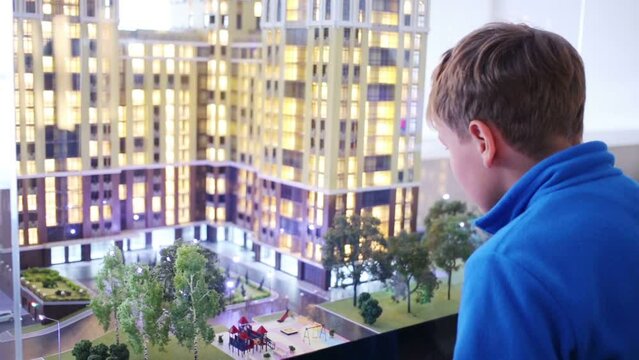Boy in blue looks at layout of buildings with illuminated windows