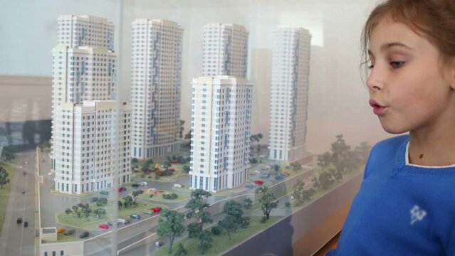 Talking girl in blue looks at layout of buildings through glass