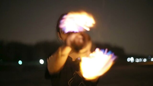 Guy rotates burning pois around his hands making spirals.