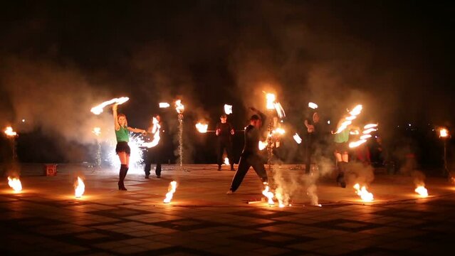 Boys spin pois and girls dance with burning fans at fireshow.