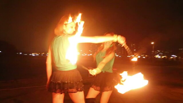 Two girls perform with burning torches at evening fire show.