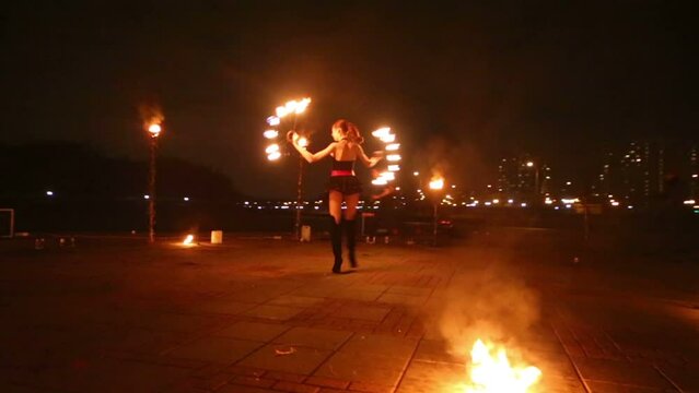 Young girl dances with burning torches shaped as fans, man behind