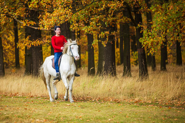 A pretty young woman and a white horse galloping along the forest path
