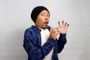 Shocked and frightened young Asian man, dressed in a beanie hat and casual shirt, reacts to...