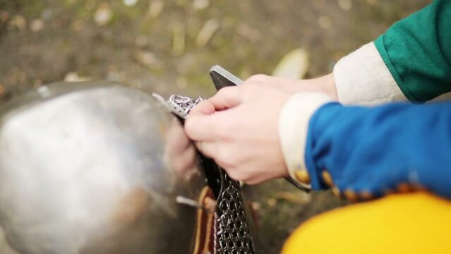 Hands of man in medieval costume repairing metal helmet